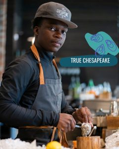 Shucker wearing True Chesapeake hat holding up an oyster
